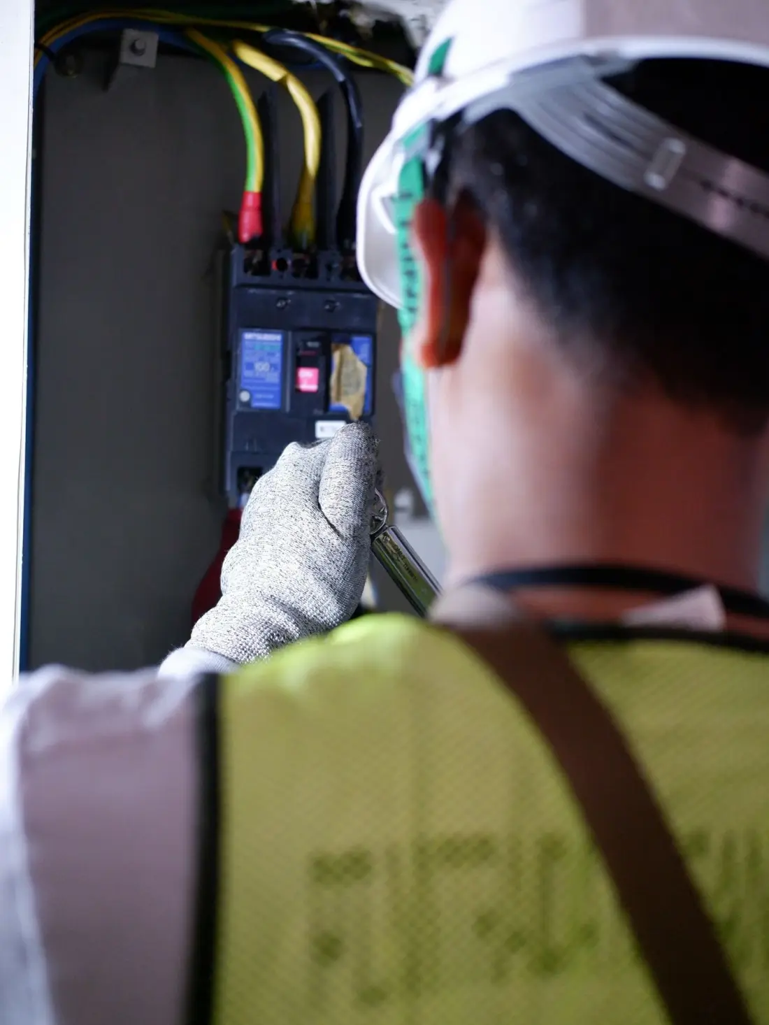 An electrician in a hi-vis vest working at a breaker panel